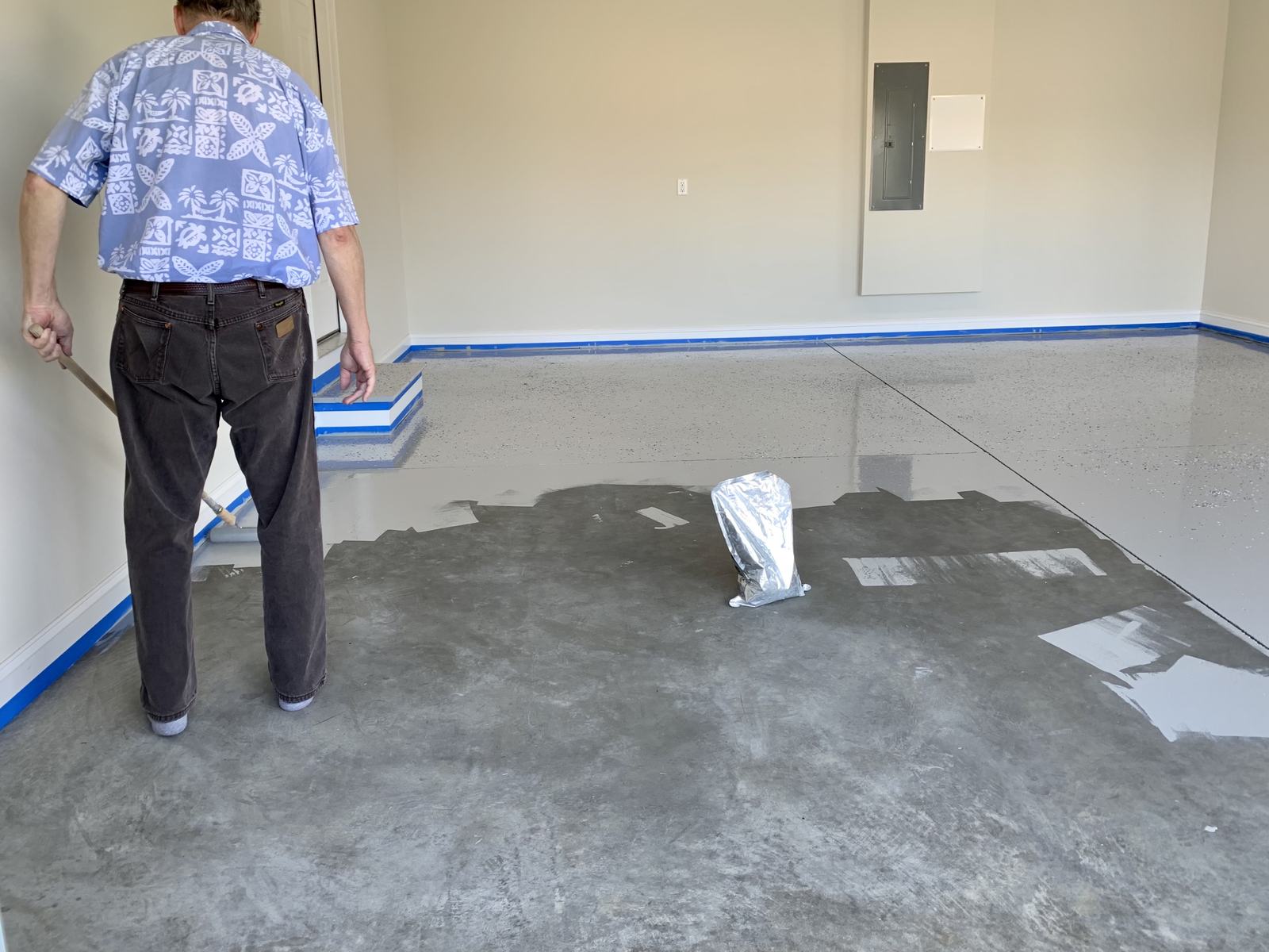 Installer spreading gray floor coating across a concrete slab with a long-handled applicator